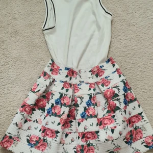 Blommig kjol från Amisu - Supersöt kjol från Amisu blommig i strukturvävt tyg. Kjolen har rosa och blå rosor på vit botten och är veckad för extra volym. Perfekt för dig som gillar färg och mönster!