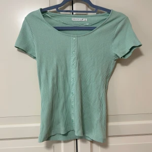 Mintgrön ribbad tröja - Superfin mintgrön topp från Black Story med ribbad struktur och knappar framtill. Modellen har korta ärmar och en rundad halsringning. Älskar modellen, men färgen passar inte mig. Aldrig använd, helt ny