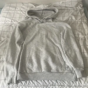 Ljusgrå hoodie från Bershka, loose fit - Ljusgrå hoodie från Bershka i loose fit med klassisk känguruficka och snörning i huvan. Mjuk insida och ribbade muddar vid ärmslut och nederkant. Perfekt för chill dagar eller när du vill ha en enkel och stilren look.