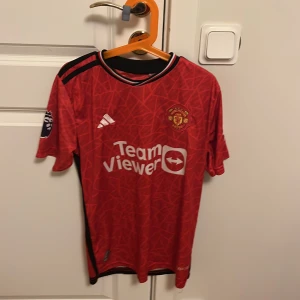 Manchester United Rashford 10 Adidas tröja - Manchester Uniteds officiella matchtröja med Rashford 10 på ryggen. Röd med svarta detaljer, vita tryck och diskret geometriskt mönster. Premier League-logga på ärmen och TeamViewer sponsor framtill. Tillverkad i lätt och ventilerande polyester. Storlek. S