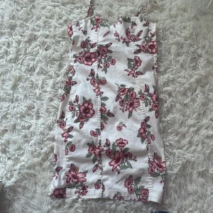 Vit blommig kortklänning H&M Divided - Supersöt vit kortklänning från H&M Divided med tunna axelband och rosa blommigt mönster. Klänningen har figurnära passform och är perfekt för varma dagar. Materialet känns lätt och somrigt, och blommorna ger en romantisk vibe.