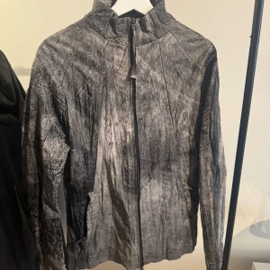 Handgjort skinnjacka från OBJECT London - Säljer en unik grå handgjord skinnjacka från OBJECT London med coolt abstrakt mönster. Jackan har hög krage, hel dragkedja framtill och långa ärmar. Materialet är 100% läder med bomullsfoder, vilket ger en schysst känsla och look.