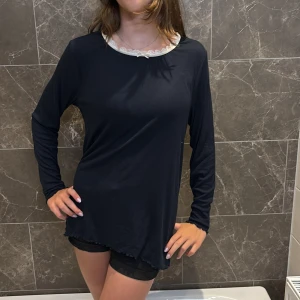 Mörkblå långärmad topp med spets - Mörkblå långärmad topp med vit spetsdetalj vid halsringningen. Modellen är rak och lite längre, med vågig kant nertill och vid ärmslut. Perfekt för dig som gillar en enkel men söt stil.