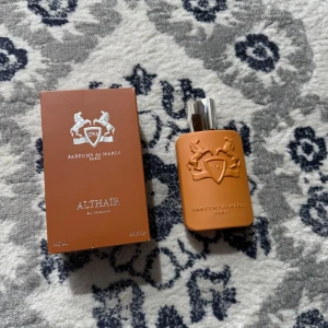 Parfums de Marly Althaïr EdP 125ml - Exklusiv parfym från Parfums de Marly, Althaïr EdP 125ml. Flaskan är mattbrun med silverdetaljer och har en elegant, modern design med reliefmönster av två hästar och logotyp. Kommer med matchande brun kartong. Perfekt för dig som gillar lyxiga dofter.