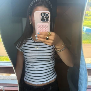 Randig croppad topp med volangkant - Säljer en vit och svart randig croppad topp med korta ärmar. Toppen har ribbad struktur och en söt volangkant längst ner. Perfekt för dig som gillar en enkel men trendig stil.OBS det är spegeln som är smutsig och inte tröjan 