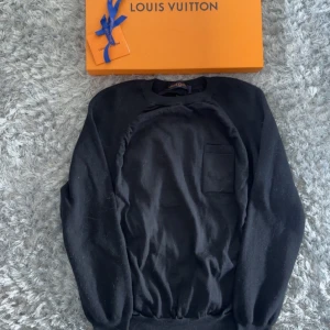 Svart stickad tröja Louis Vuitton M - Exklusiv svart stickad tröja från Louis Vuitton med broderad logga på bröstfickan. Tröjan har rund halsringning, långa ärmar och ribbade muddar. Tillverkad i Italien och perfekt för dig som gillar stilrena designer med lyxig känsla.