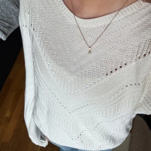 Vit stickad tröja med mönster - Vit stickad tröja med snyggt V-format hålmönster över hela framsidan. Tröjan har rund halsringning, långa ärmar och ribbade muddar vid ärmslut och nederkant. Perfekt att styla med jeans för en clean look.