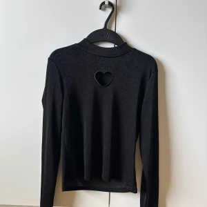 Svart långärmad topp med hjärtformad detalj - Svart långärmad topp från Monki med en unik hjärtformad cut-out i ryggen. Tight passform och mjukt stretchigt material som sitter snyggt. Perfekt för dig som vill ha en basic topp med en söt twist.