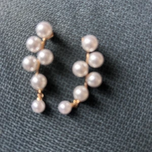 Örhängen med vita pärlor - Säljer ett par snygga örhängen med vita pärlor i rad på tunn guldfärgad stomme. De har en elegant och stilren design som ger en lyxig känsla. Perfekta för att lyfta vilken outfit som helst med en touch av klass.