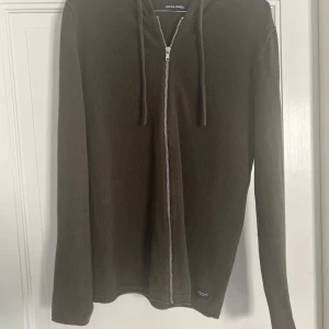 Jack & Jones stickad hoodie med zip dragkedja - Snygg stickad hoodie från Jack & Jones med dragkedja framtill och huva med snörning. Finns i både mörkgrön och mörkblå färg. Perfekt för dig som gillar en enkel men stilren look. Långärmad modell i mjukt stickat material. Perfekt nu till hösten! Vill du ha båda kan jag komma på en paket deal. Storlek S men passar även M