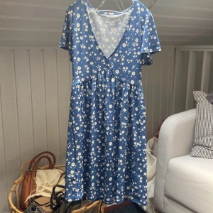 Blå blommig kortklänning med v-ringning - Kort blå klänning med små vita blommor. Aldrig använd men prislappen är borttagen. 