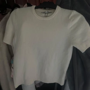 Vit stickad kortärmad tröja från Zara - Superfin vit stickad tröja från Zara med korta ärmar och rund halsringning. Tröjan har ribbade muddar vid ärmslut och nederkant, vilket ger en snygg och enkel look. Perfekt att styla med jeans eller kjol för en clean vibe.