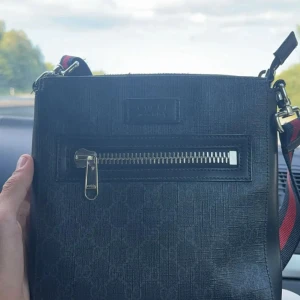 Gucci GG supreme - Snygg svart axelväska från Gucci med diskret GG-mönster i tyget och silverfärgad dragkedja framtill. Väskan har justerbar axelrem med röd och marinblå detalj. Tillverkad i slitstarkt material med läderdetaljer och präglad logotyp på framsidan.