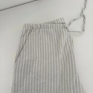 Randiga linnebyxor från Gina Tricot - Snygga ljusgrå linnebyxor från Gina Tricot med vita ränder. Byxorna har elastisk midja med snörning och raka ben. Storlek 170 från barnavdelningen. Skulle säga att de passar en Xs damstorlek. Byxorna är aldrig använda. Nypris 400kr