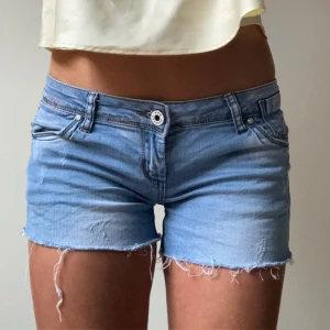 Lågmidjade ljusblå jeansshorts - Lågmidjade ljusblå jeansshorts med slitningar i lite strechigare material men fortfarande denim känsla. Midjemått 36.5cm passar en S/M. Postar snabbt!