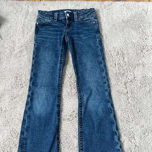 Blå bootcut jeans Gina Tricot 146 - Snygga blå jeans från Gina Tricot i storlek 146. Modellen har bootcut-ben, klassiska fem fickor och coola detaljer på bakfickorna med knappar. Jeansen är i stretchigt denim och har normal passform. Perfekta för en chill och trendig look.