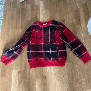 Rutig röd stickad tröja från H&M - Säljer en supermysig stickad tröja från H&M i rött, svart och rosa rutigt mönster. Tröjan har rund halsringning, långa ärmar och ribbade muddar. Perfekt för dig som vill ha en färgstark och skön look under kyliga dagar.