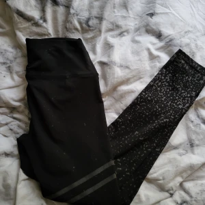 Svarta leggings med mönster - Snygga svarta leggings med hög midja och coolt guldigt mönster nertill på benen. Två guldiga ränder på ena benet ger extra sportig vibe. Perfekta för träning eller chill. Stretchigt material som sitter skönt och följer kroppen.