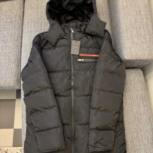 Svart pufferjacka från Pr4da - Snygg svart pufferjacka från Pr4da med långärmad design och dragkedja. Jackan har en quiltad stil och är fodrad med mjuk päls på insidan för extra värme. Perfekt för kyliga dagar.