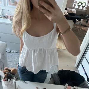 Vit ärmlös linnetopp - Säljer en söt vit ärmlös linnetopp med en luftig passform. Toppen har en knytning i ryggen som ger en fin detalj. Perfekt för varma sommardagar!