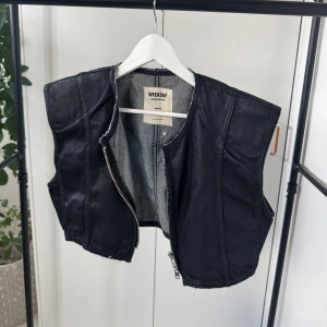 Svart jeansväst från Weekday - Snygg svart jeansväst från Weekday med dragkedja framtill. Västen har en cool, croppad design och är perfekt för att ge din outfit en edgy touch.