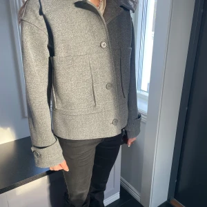 Grå kappa från Kappahl  - Snygg grå kappa från H&M med stora knappar och två framfickor. Jackan har en klassisk krage och långa ärmar. Perfekt för kyligare dagar. Helt ny i den är aldrig använd, nypriset var ungefär 900