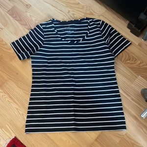 Svart och vit randig topp - Säljer en svart och vit randig topp med korta ärmar. Perfekt för en avslappnad stil. Toppen har en klassisk rund halsringning och är gjord i ett mjukt material.