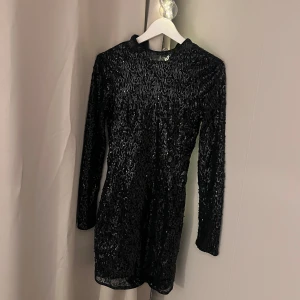 Svart glittrig klänning - Snygg svart klänning med glittrande yta från Gina tricot. Den har en kort längd och långa ärmar, perfekt för en kväll ute. Klänningen är i ett stretchigt material. 