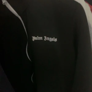 Svart vindjacka från Palm Angels - Snygg svart vindjacka från Palm Angels med vit dragkedja och logga på bröstet. Perfekt för en stilren look.