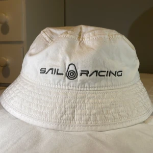 Vit hatt från Sail Racing - Snygg vit hatt från Sail Racing med broderad logga framtill. Perfekt för soliga dagar med sin klassiska design och bekväma passform. Tillverkad i bomull för en lätt och luftig känsla. Ganska liten i storleken pris kan diskuteras 
