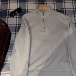 Ljusblå tröja med dragkedja - Säljer en stilren ljusblå tröja med halv dragkedja och hög krage. Perfekt för kyligare dagar med sin långa ärmar och mjuka material. Enkelt att matcha med olika outfits.