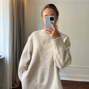 Beige stickad polotröja - Säljer en stilren beige stickad polotröja med ribbade detaljer vid ärmslut och nederkant. Tröjan har en hög krage och långa ärmar, perfekt för kyligare dagar. Passar både till jeans och kjol för en avslappnad look.