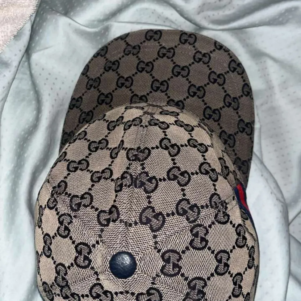 Snygg beige keps från Gucci med det ikoniska GG-monogrammet över hela ytan. Kepsen har en klassisk design med en röd och blå randdetalj på sidan. Perfekt för att ge din outfit en lyxig touch.. Asusteet.