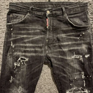 Svarta Dsquared2 Jeans - Säljer ett par svarta jeans med slitningar och distressed detaljer. De har en klassisk femficksdesign och knappgylf. Perfekta för en edgy look. STORLEK 50