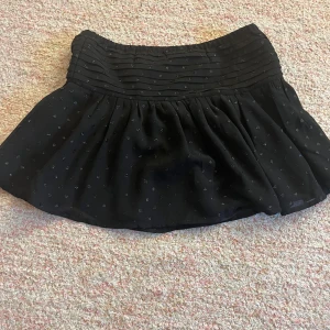 Svart kortkjol från Gina Tricot - Säljer en söt svart kortkjol från Gina Tricot med små glittriga prickar och veckad detalj upptill. Perfekt för att ge en touch av glitter till din outfit. Kjolen har en bekväm passform och är lätt att matcha med olika toppar.