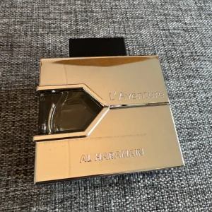 L'Aventure Al Haramain Parfym - Upptäck L'Aventure från Al Haramain, en maskulin parfym med en fräsch och kryddig doftprofil. Toppnoterna av citron, bergamott och elemi ger en citrusaktig start, medan hjärtnoterna av trä, jasmin och liljekonvalj tillför en blommig och träig karaktär. Basnoterna av mysk, patchouli och amber ger en varm och sensuell avslutning. Använd ett par ggr, så ca 98ml kvar. Lådan medföljer ej.