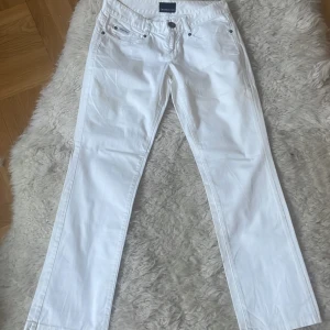 Vita jeans från Calvin Klein st. S - Snygga vita jeans från Calvin Klein med klassisk femficksdesign och knappgylf. Perfekta för en stilren look. De har en rak passform och är tillverkade i ett bekvämt material. Midjemått 80 cm, Innebensmått 73 cm.