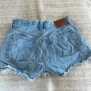 Blå jeansshorts med fransar - Snygga blå jeansshorts från Levi's med fransiga kanter och klassisk femficksdesign. Perfekta för en avslappnad sommarlook. De har en knappgylf och är högmidjade för en bekväm passform.