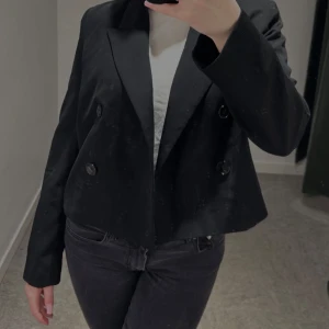 Svart kort trenchcoat  - Snygg svart trench med dubbelknäppning och en croppad design. Perfekt för en stilren look. Passar bra till både jeans och kjol.