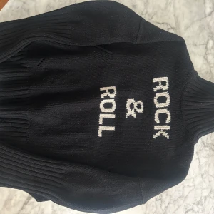 Svart stickad tröja från Zadig & Voltaire - Säljer en svart stickad tröja från Zadig & Voltaire med texten 'Rock & Roll' . 100% ull. Tröjan har en hög krage och långa ärmar, perfekt till jeans för en hastigare look eller till en kjol på sommarkvällar. Passar från xs-m. Använd några gånger, jättebra skick (bara lite noppor som en noppmaskin tar bort busenkelt). Köpt för 325€. 