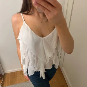 Vit volangtopp från Zara - Säljer en söt vit topp från Zara med tunna axelband och volangdetaljer. Endast använd en gång så den är som ny💓
