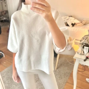 Vit kortärmad tröja - Säljer en stilren vit tröja med korta ärmar och hög krage. Perfekt för en avslappnad look. Tröjan har en lös passform och är tillverkad i ett mjukt material.