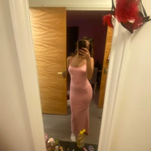 Rosa långklänning - Säljer en elegant rosa långklänning med smala axelband. Klänningen har en figurnära passform som framhäver silhuetten. Perfekt för speciella tillfällen.