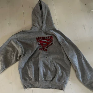 Grå hoodie från Jerzees - Säljer en grå hoodie från Jerzees med en stor ficka framtill och tryck på bröstet. Huvan är rymlig och bekväm.