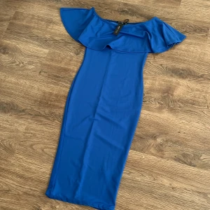 Blå offshoulder klänning från NLY One - Snygg blå offshoulder klänning från NLY One med volangdetalj. Perfekt för en stilren look. Klänningen har en smickrande passform och är tillverkad i ett mjukt material.