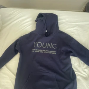 Mörkblå hoodie med text - Säljer en mörkblå hoodie med texten 'YOUNG' på framsidan. Hoodien har en klassisk design med en stor ficka framtill och en bekväm huva. Perfekt för en avslappnad stil.