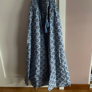 Mönstrad långkjol från Gina Tricot - Säljer en vacker långkjol från Gina Tricot med ett blått och vitt mönster. Kjolen har en elastisk midja och dekorativa tofsar. Perfekt för en bohemisk look! Använd 2 gånge och köpt för 200