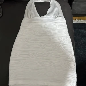 Vit klänning med öppen rygg - Snygg vit klänning med en stilren design och öppen rygg. Klänningen har en halterneck-stil och är perfekt för sommarens fester. Materialet har en subtil textur som ger en extra touch.