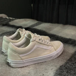 Beige sneakers från Vans - Säljer ett par klassiska beige sneakers från Vans med vit sula och snörning. Skorna har den ikoniska sidostripen i vitt och är perfekta för en avslappnad stil. Passar bra till både jeans och shorts.storlek 37 Skorna är använda men annars i väldigt fint skick!!