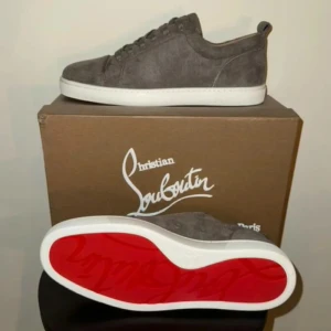 Grå sneakers från Christian Louboutin - Snygga grå sneakers i mocka från Christian Louboutin med den ikoniska röda sulan. Skorna har snörning och en vit sula som ger en stilren look. Perfekta för dig som vill ha en touch av lyx i vardagen.